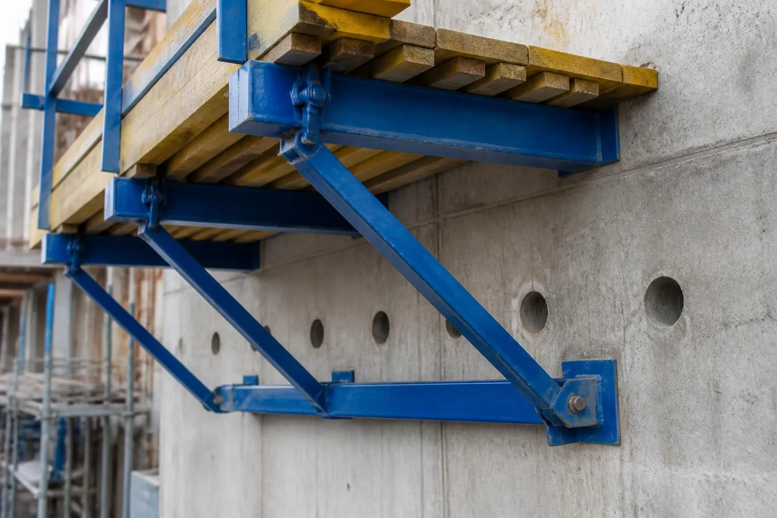 Console de coffrage grimpant accrochée à un voile de béton brut, platelage de passerelle et réservations d’ancrage alignées