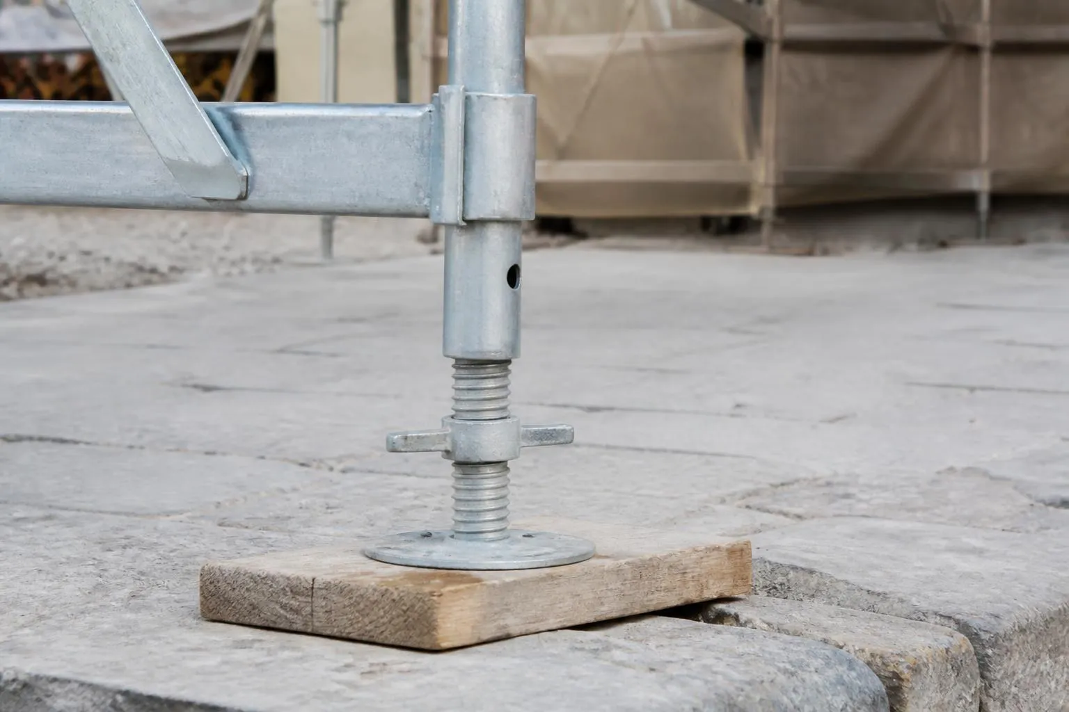 Vérin de pied réglable vissé sur une cale de bois, au départ d’une file d’échafaudage de façade
